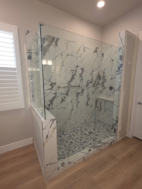Frameless glass shower enclosure with river-stone floor and marble-veined tile installed in Indio, CA